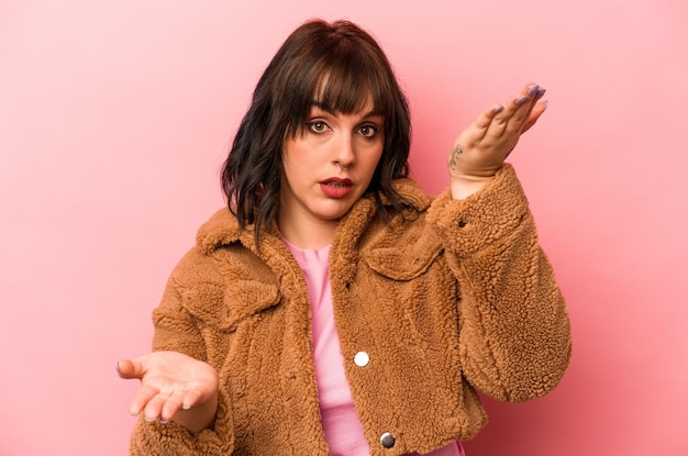 Young caucasian woman isolated on pink background makes scale with arms feels happy and confident