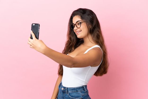 Young caucasian woman isolated on pink background making a selfie