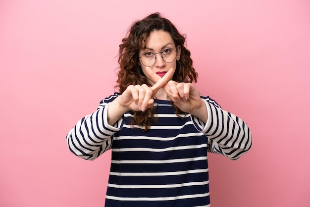 Young caucasian woman isolated on pink background making stop\
gesture with her hand to stop an act