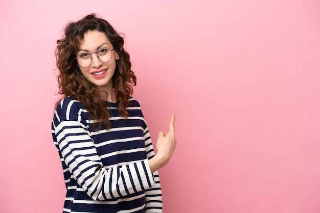 Young caucasian woman isolated on pink background pointing back