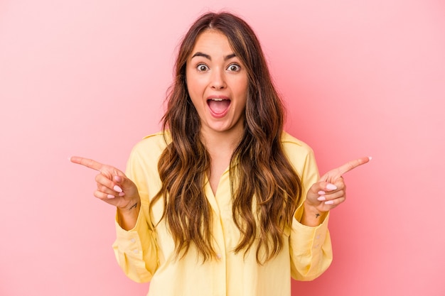 Young caucasian woman isolated on pink background pointing to different copy spaces, choosing one of them, showing with finger.