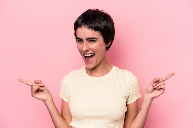 Young caucasian woman isolated on pink background pointing to different copy spaces, choosing one of them, showing with finger.