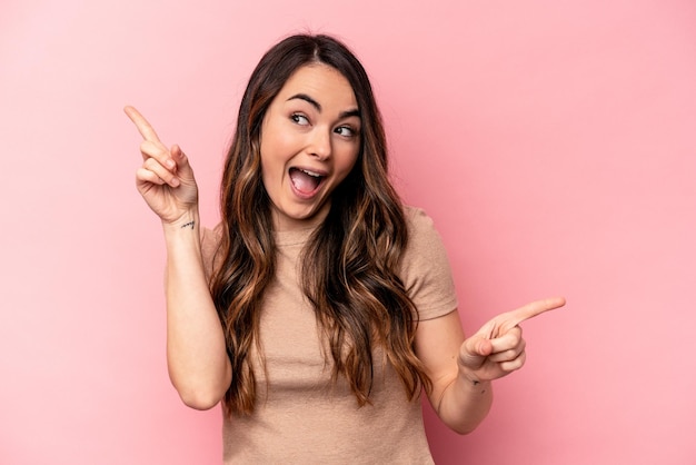 Young caucasian woman isolated on pink background pointing to different copy spaces choosing one of them showing with finger