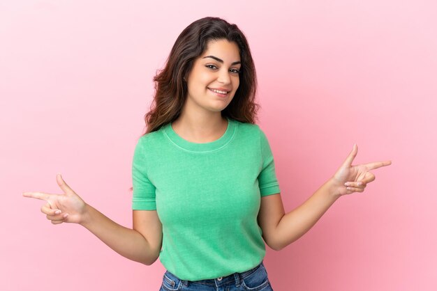 Young caucasian woman isolated on pink background pointing finger to the laterals and happy