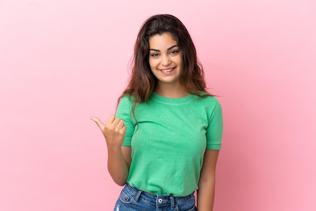 Young caucasian woman isolated on pink background pointing to the side to present a product