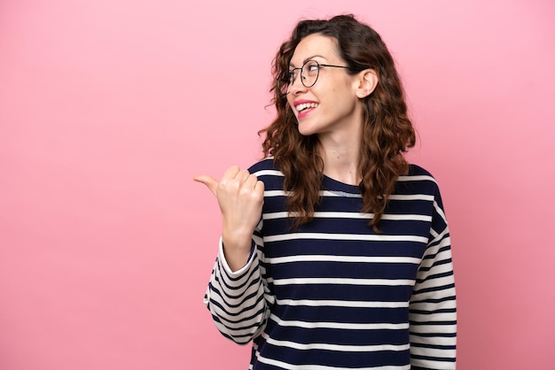 Young caucasian woman isolated on pink background pointing to the side to present a product