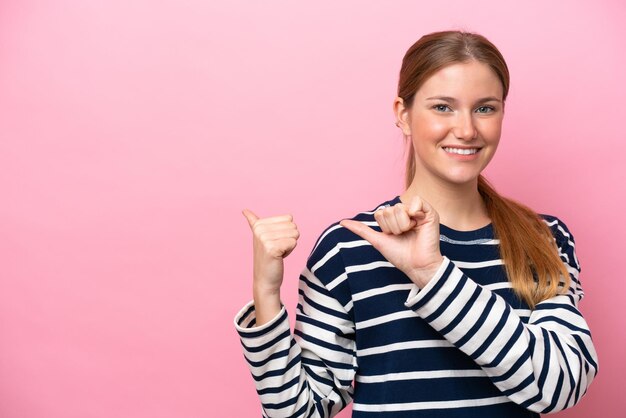 Foto giovane donna caucasica isolata su sfondo rosa che punta al lato per presentare un prodotto