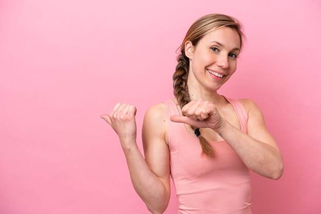 Young caucasian woman isolated on pink background pointing to the side to present a product