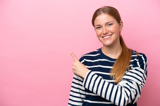 製品を提示する側を指しているピンクの背景に分離された若い白人女性