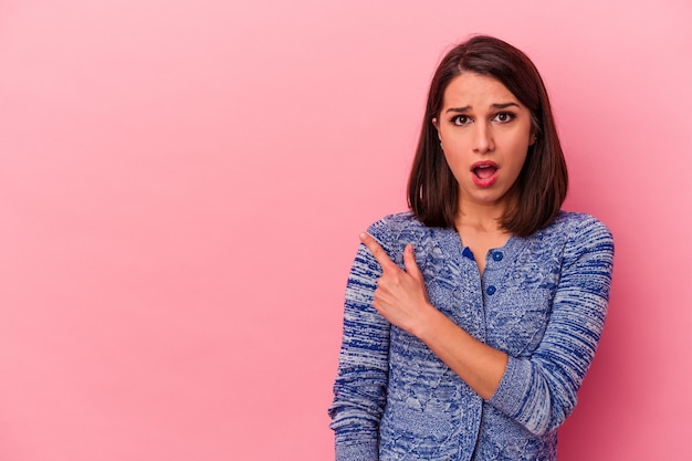 Young caucasian woman isolated on pink background pointing to the side