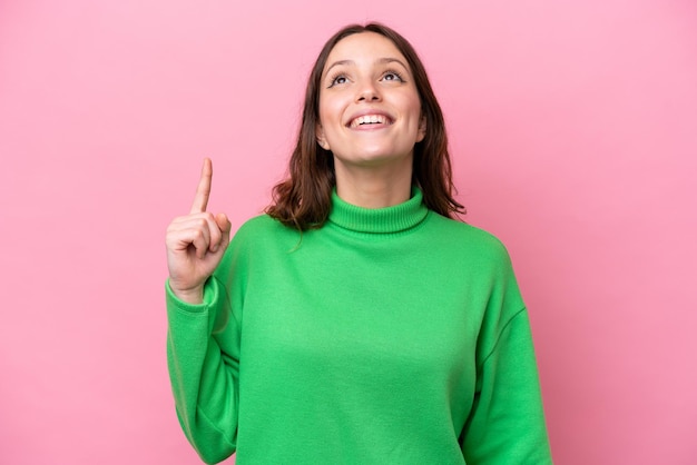 Young caucasian woman isolated on pink background pointing up and surprised