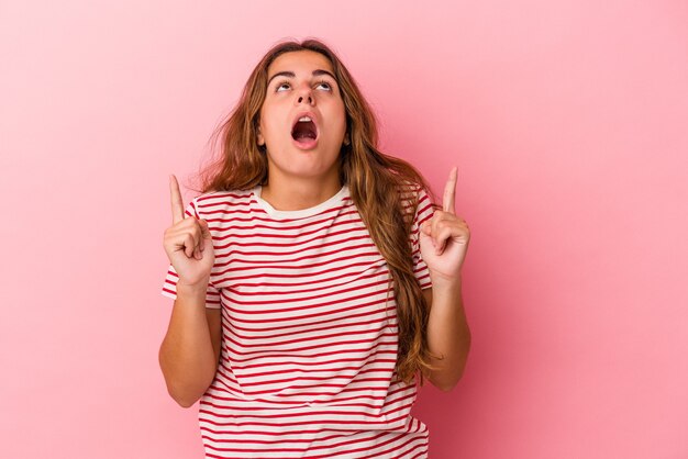 Young caucasian woman isolated on pink background  pointing upside with opened mouth.