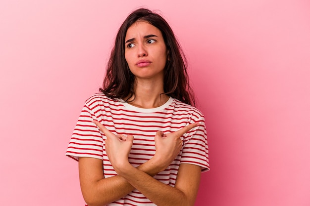 Young caucasian woman isolated on pink background points sideways, is trying to choose between two options.