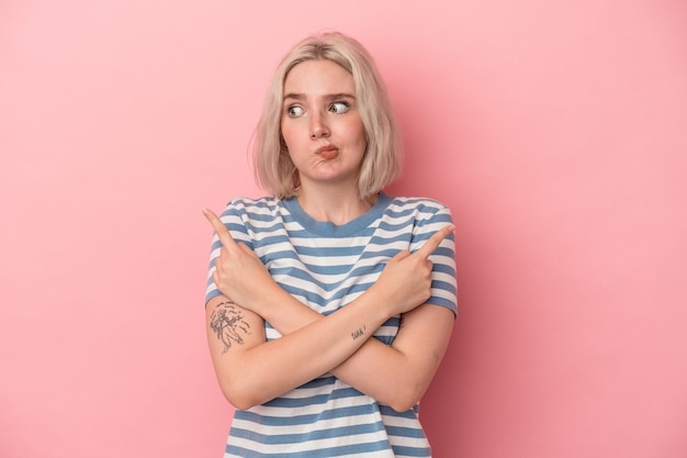 Young caucasian woman isolated on pink background points sideways, is trying to choose between two options.