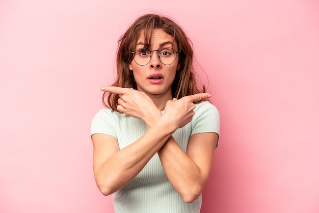 Young caucasian woman isolated on pink background points sideways is trying to choose between two options