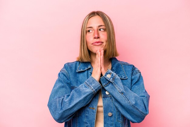 Young caucasian woman isolated on pink background praying showing devotion religious person looking for divine inspiration