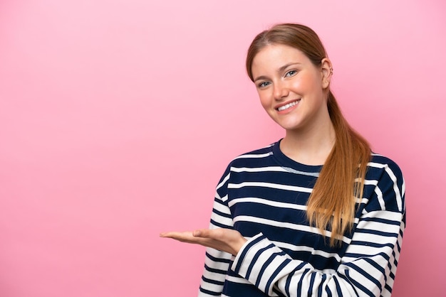 Young caucasian woman isolated on pink background presenting an idea while looking smiling towards