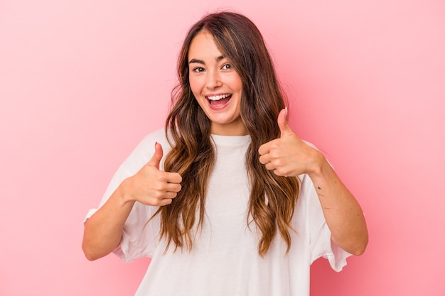 Young caucasian woman isolated on pink background raising both thumbs up, smiling and confident.