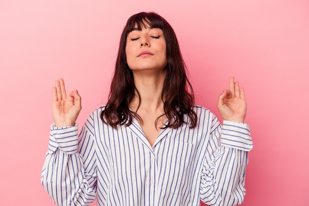 Young caucasian woman isolated on pink background relaxes after hard working day, she is performing yoga.