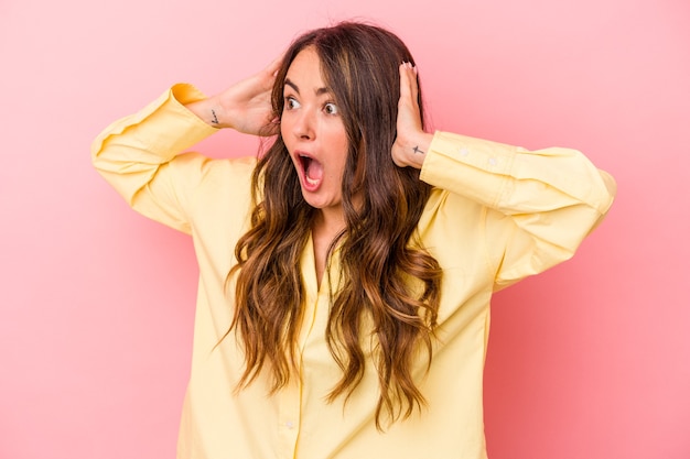 Young caucasian woman isolated on pink background screaming, very excited, passionate, satisfied with something.