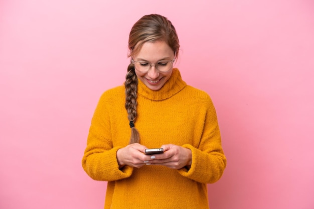 Young caucasian woman isolated on pink background sending a message with the mobile