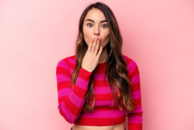 Young caucasian woman isolated on pink background shocked covering mouth with hands anxious to discover something new