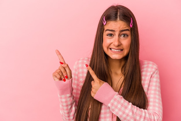 Young caucasian woman isolated on pink background shocked pointing with index fingers to a copy space.