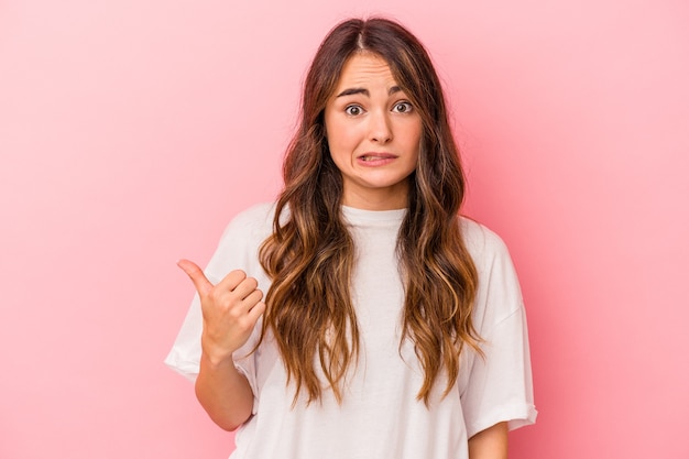 Young caucasian woman isolated on pink background shocked pointing with index fingers to a copy space.