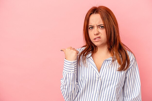 Young caucasian woman isolated on pink background shocked pointing with index fingers to a copy space.