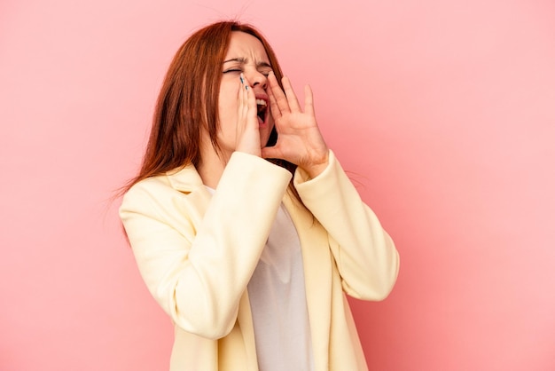 분홍색 배경에 격리된 젊은 백인 여성이 앞으로 흥분해서 소리를 질렀습니다.