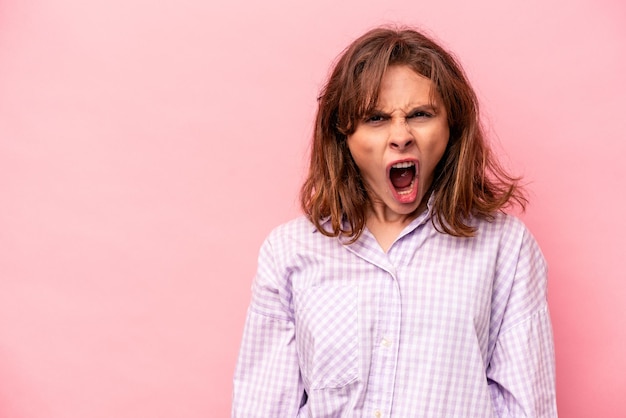 Young caucasian woman isolated on pink background shouting very angry rage concept frustrated