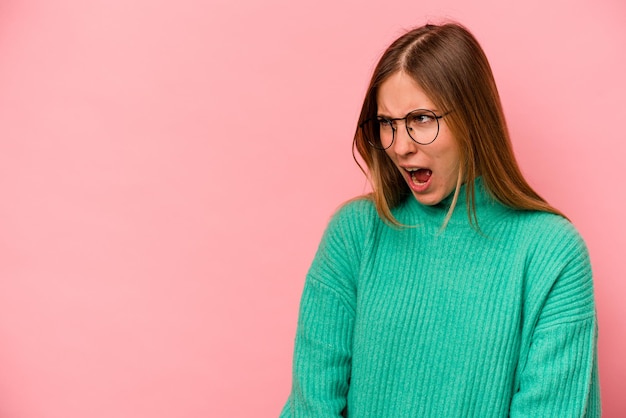 Young caucasian woman isolated on pink background shouting very angry rage concept frustrated