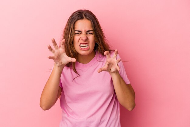 고양이, 공격적인 제스처를 모방 하는 발톱을 보여주는 분홍색 배경에 고립 된 젊은 백인 여자.