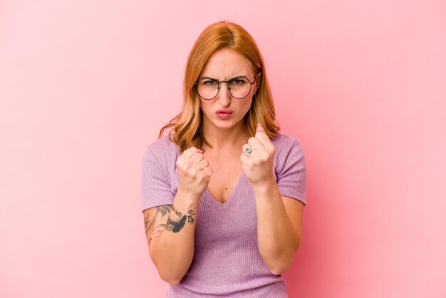 Young caucasian woman isolated on pink background showing fist to camera, aggressive facial expression.