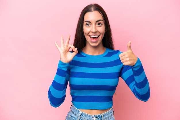 Young caucasian woman isolated on pink background showing ok sign and thumb up gesture