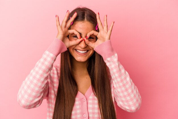 Young caucasian woman isolated on pink background showing okay sign over eyes