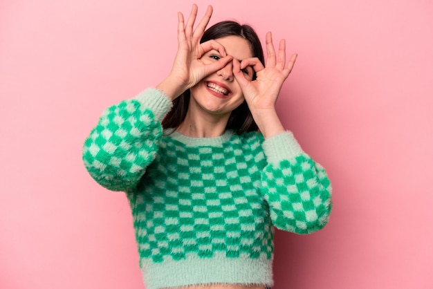 Young caucasian woman isolated on pink background showing okay sign over eyes