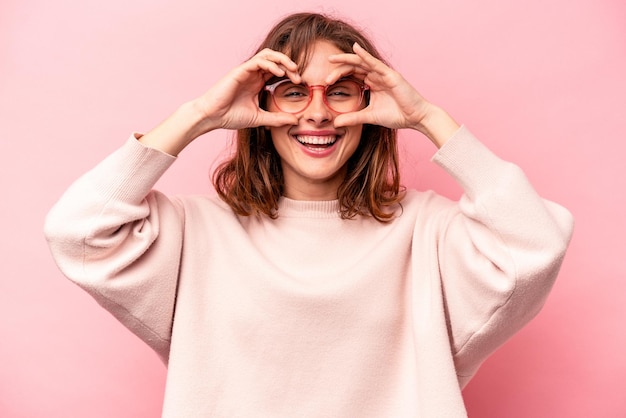 Young caucasian woman isolated on pink background showing okay sign over eyes