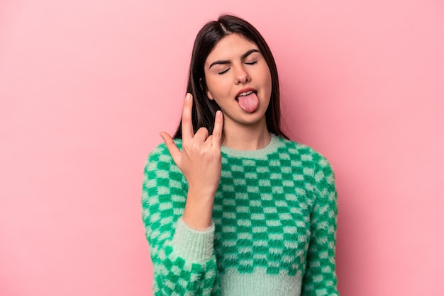 Young caucasian woman isolated on pink background showing rock gesture with fingers