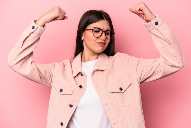 Giovane donna caucasica isolata su sfondo rosa che mostra gesto di forza con le braccia simbolo del potere femminile