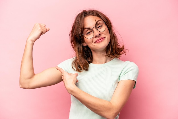 Young caucasian woman isolated on pink background showing strength gesture with arms symbol of feminine power