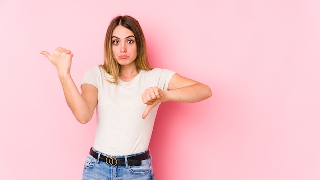 Young caucasian woman isolated on pink background showing thumbs up and thumbs down, difficult choose concept