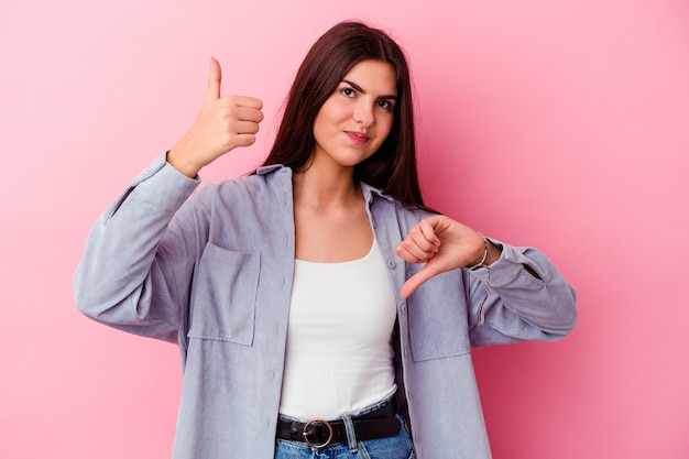 Young caucasian woman isolated on pink background showing thumbs up and thumbs down, difficult choose concept