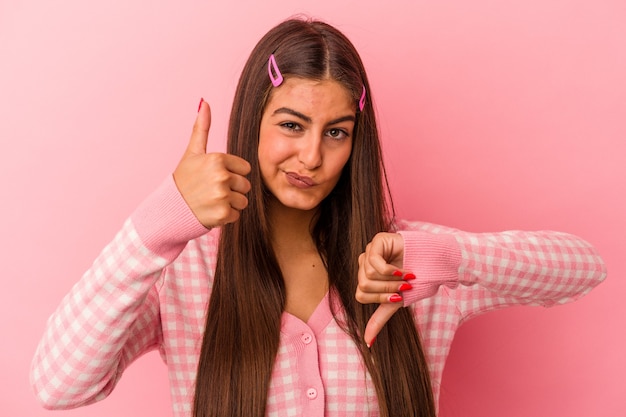 Foto giovane donna caucasica isolata su sfondo rosa che mostra pollice in alto e pollice in basso, difficile scegliere il concetto