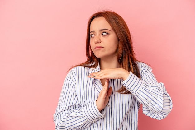 young caucasian woman isolated on pink background showing a timeout gesture.