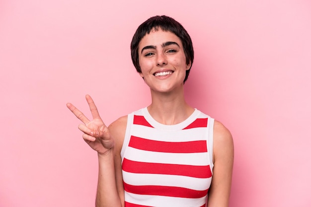 Young caucasian woman isolated on pink background showing victory sign and smiling broadly