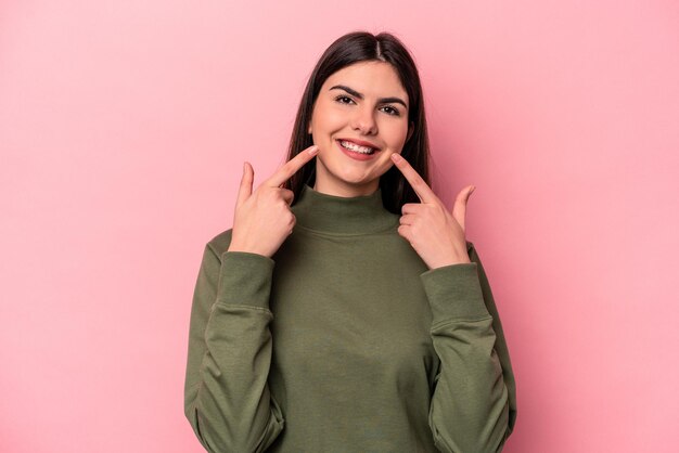 Young caucasian woman isolated on pink background smiles pointing fingers at mouth