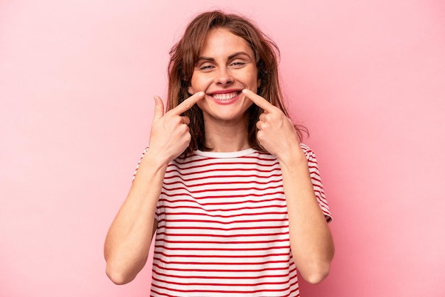 Young caucasian woman isolated on pink background smiles pointing fingers at mouth