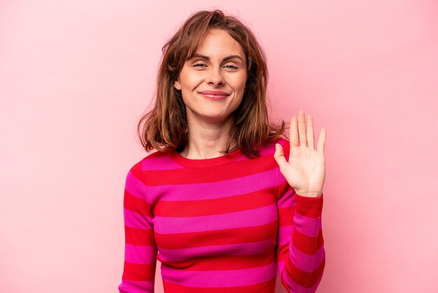 Young caucasian woman isolated on pink background smiling cheerful showing number five with fingers