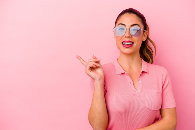 Young caucasian woman isolated on pink background smiling cheerfully pointing with forefinger away.